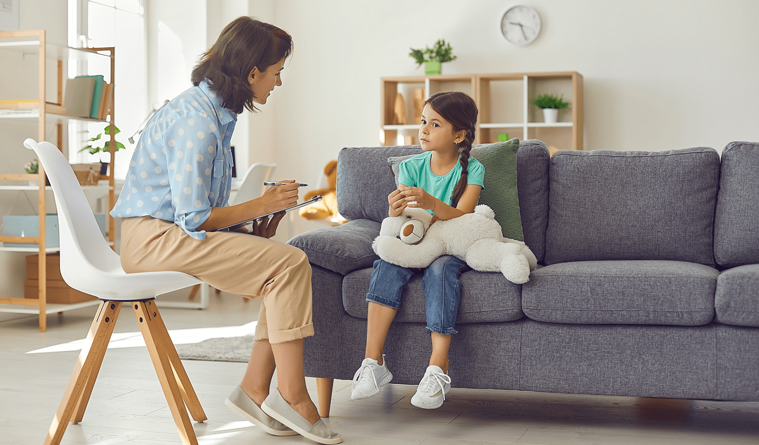 Woman talking with girl holding teddy on couch