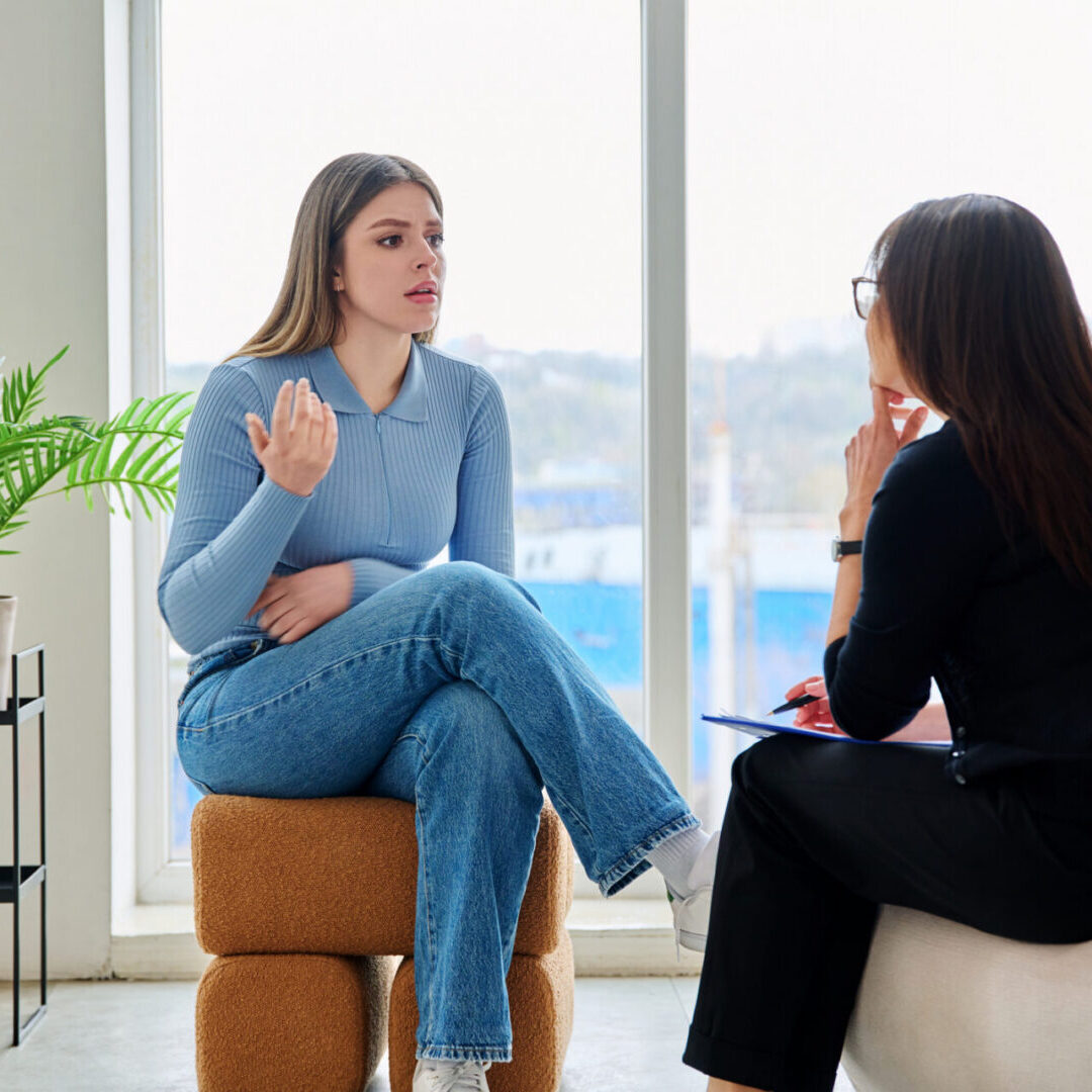 Young woman in therapy session talking with psychotherapist counselor psychologist psychoanalyst social worker. Mental health, professional psychological counseling, social services for youth students